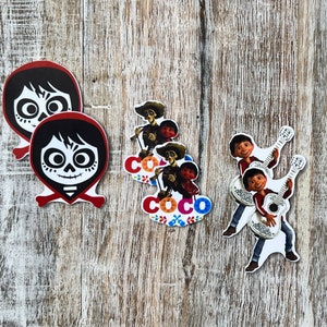 May include: A set of five colorful paper cutouts featuring characters from the animated film Coco. The cutouts include Miguel, Hector, and Dante. The cutouts are perfect for decorating a party or adding a touch of whimsy to a room.