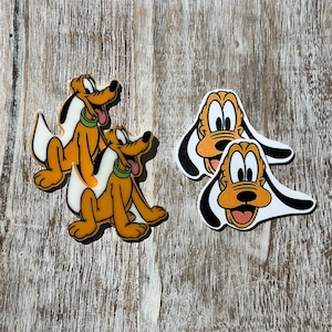 May include: Two sets of Goofy dog character iron-on patches. One set features Goofy in a sitting position with his tongue sticking out. The other set features Goofy's face with his tongue sticking out.