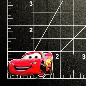 Puede incluir: Un coche de carreras rojo de dibujos animados con una cara sonriente y el n&uacute;mero 95 en el lateral. El coche tiene neum&aacute;ticos negros y una llanta blanca con la palabra "YEAR" en ella.