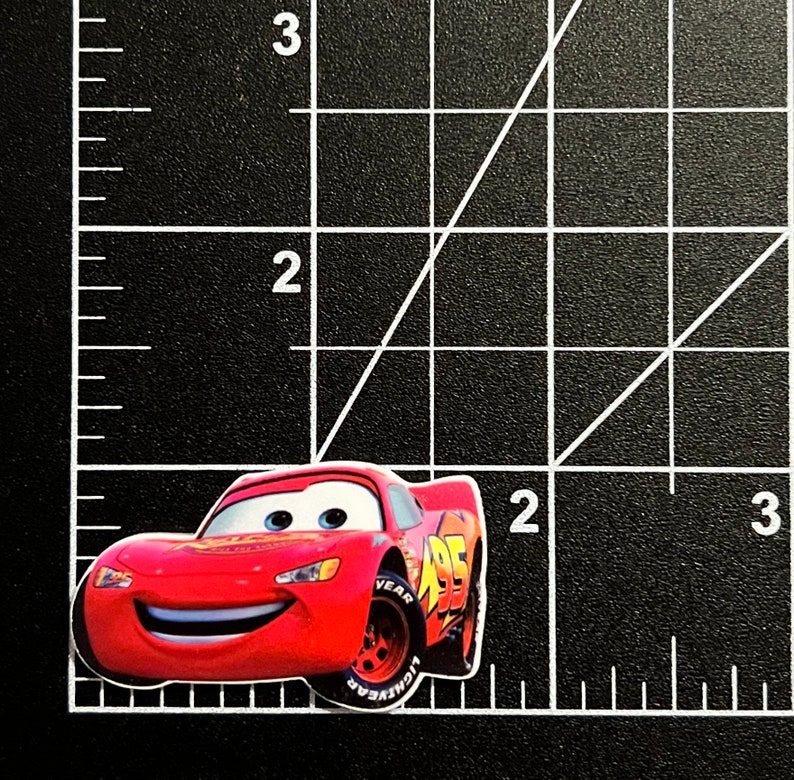 Puede incluir: Un coche de carreras rojo de dibujos animados con una cara sonriente y el n&uacute;mero 95 en el lateral. El coche tiene neum&aacute;ticos negros y una llanta blanca con la palabra "YEAR" en ella.