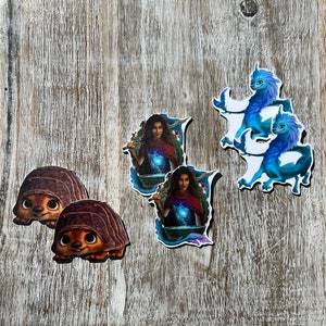 May include: Four colorful stickers featuring a woman with long dark hair, a blue dragon, and two brown turtles. The woman is wearing a red dress and holding a staff. The dragon is flying in the air. The turtles are on the ground.