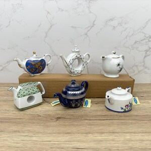 Puede incluir: Seis teteras de porcelana en miniatura con varios dise&ntilde;os y colores. Las teteras est&aacute;n dispuestas sobre una superficie de madera. Las teteras son todas de diferentes formas y tama&ntilde;os.
