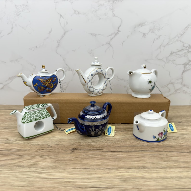 Puede incluir: Seis teteras de porcelana en miniatura con varios dise&ntilde;os y colores. Las teteras est&aacute;n dispuestas sobre una superficie de madera. Las teteras son todas de diferentes formas y tama&ntilde;os.