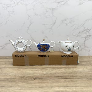Puede incluir: Tres teteras de porcelana blanca con dise&ntilde;os azules y dorados. Las teteras est&aacute;n etiquetadas como "MODEL-4", "MODEL-5" y "MODEL-6".