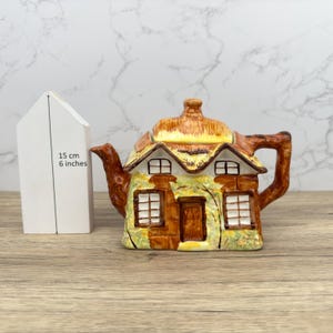 Puede incluir: Una tetera de cerámica con forma de casa de campo, con tejado de paja y ventanas. La tetera está pintada en tonos marrones, amarillos y verdes. La altura es de 15 cm (6 pulgadas).