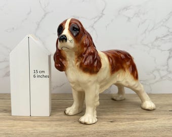 Peut inclure: Une figurine en céramique d'un cocker spaniel brun et blanc. La figurine mesure 15 cm de haut et est posée sur une surface en bois.