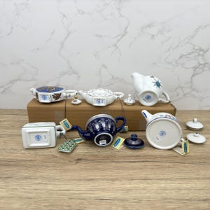 Puede incluir: Una colecci&oacute;n de seis teteras de porcelana en miniatura con varios dise&ntilde;os azules y blancos. Las teteras est&aacute;n dispuestas sobre una superficie de madera con sus fondos mirando hacia la c&aacute;mara. Cada tetera tiene una peque&ntilde;a etiqueta adjunta.