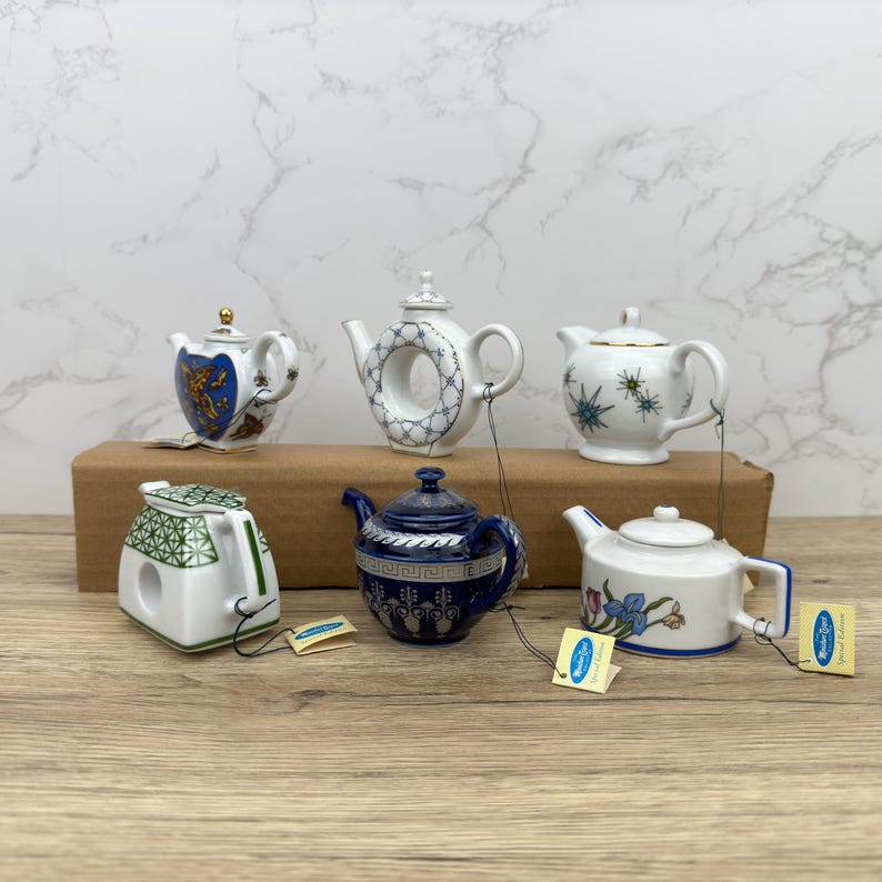 Puede incluir: Seis teteras de porcelana en miniatura con varios dise&ntilde;os y colores. Las teteras est&aacute;n colgadas de una cuerda y se muestran sobre una superficie de madera.