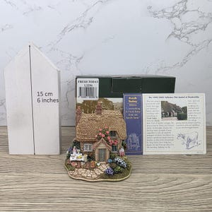 Könnte beinhalten: Detaillierte Miniatur-Cottage-Figur mit Strohdach, umgeben von Blumen und Grün. Die Figur wird von einer Schachtel und einer Karte begleitet. Die Schachtel ist mit "FRESH TODAY 1.2256" beschriftet. Die Höhe der Box beträgt 15 cm.