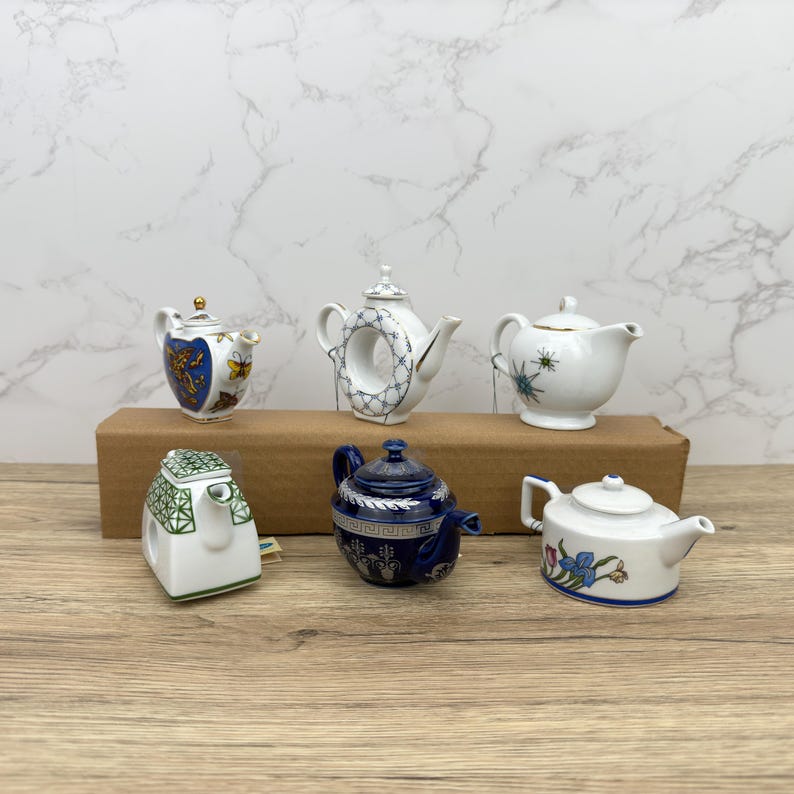 Puede incluir: Seis teteras de porcelana en miniatura en varios colores y dise&ntilde;os. Las teteras est&aacute;n dispuestas sobre una superficie de madera.