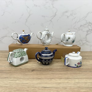 Puede incluir: Seis teteras de porcelana en miniatura en varios colores y dise&ntilde;os. Las teteras est&aacute;n dispuestas sobre una superficie de madera.