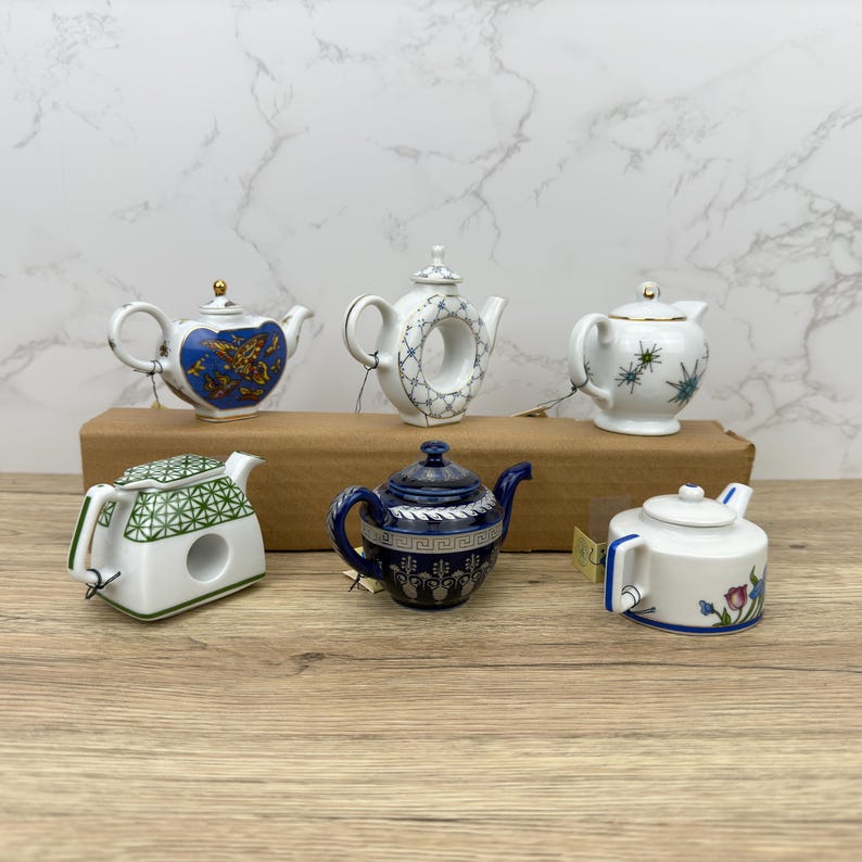 Puede incluir: Seis teteras de porcelana en miniatura en varios colores y dise&ntilde;os. Las teteras est&aacute;n dispuestas sobre una superficie de madera.