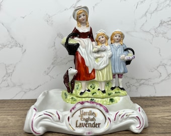 Puede incluir: Un joyero de porcelana con una madre y dos niños con cestas de flores. El joyero está decorado con un diseño floral verde y morado y tiene una etiqueta ovalada con borde dorado que dice "Yardley English Lavender".