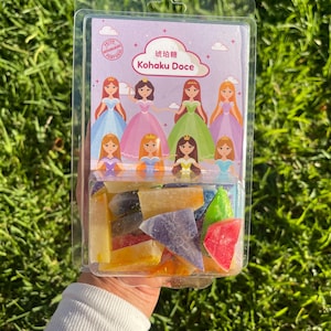 Könnte beinhalten: Eine durchsichtige Kunststoff-Blisterverpackung mit mehrfarbigen, kristallin strukturierten Bonbonstücken. Die Verpackung zeigt ein Etikett mit acht illustrierten Prinzessinnen in bunten Kleidern und den Text "琥珀糖 Kohaku Doce".