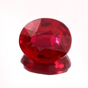 Può includere: Una gemma di rubino dal taglio ovale con un colore rosso intenso e saturo. La pietra presenta una superficie sfaccettata con molteplici piani geometrici che riflettono la luce, creando una brillantezza interna e un contorno netto e preciso.