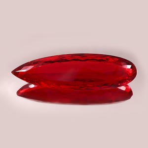 May include: A faceted, teardrop-shaped gemstone in a vibrant, deep red hue. The gem is highly polished, reflecting light and creating a brilliant sparkle. The stone is displayed against a soft, neutral background, with its reflection visible below.