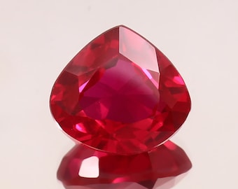 Puede incluir: Una gema de rubí facetada en forma de corazón. La gema es de un color rojo intenso y vibrante con una superficie pulida, que refleja la luz. El rubí se asienta sobre una superficie reflectante, creando un efecto de espejo. Adecuado para la fabricación de joyas.