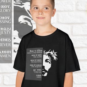 May include: Black t-shirt with a white image of Jesus Christ wearing a crown of thorns. The text on the shirt reads "Φωκ τε Χοu THINE IS THE POWER ΝΕΜ ΠΙ ΜΟΥ, THE GLORY ΝΕΜ ΠΙΣΜΟΥ, THE BLESSING THE MAJESTY A ENER FOREVER ΣΜΗΝ AMEN".