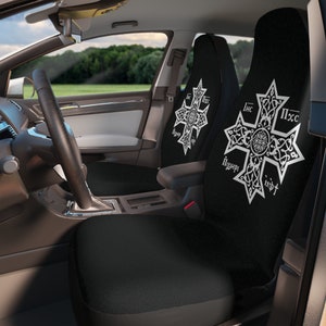 May include: Two black car seat covers with white embroidered crosses. The crosses have intricate designs and the text "IHC NIKA" and "IHC XC" in a stylized font.