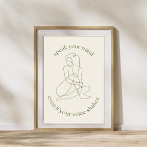 Può includere: Una stampa incorniciata con un disegno di linea minimalista di una persona seduta con il testo "speak your mind even if your voice shakes" in verde.