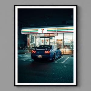 Peut inclure: Impression encadrée d'une voiture de sport bleue garée devant un magasin 7-Eleven la nuit. L'enseigne du magasin est éclairée et les feux arrière de la voiture sont allumés. La plaque d'immatriculation japonaise est visible.