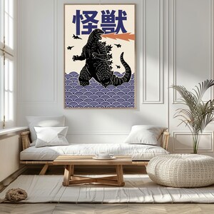 以下が含まれることがあります： 黒いゴジラのイラストとオレンジ色の火の息、日本語のテキストが描かれた額入りのアートプリント。アートワークは、青い波模様のクリーム色の背景に配置されています。プリントはリビングルームに展示されています。