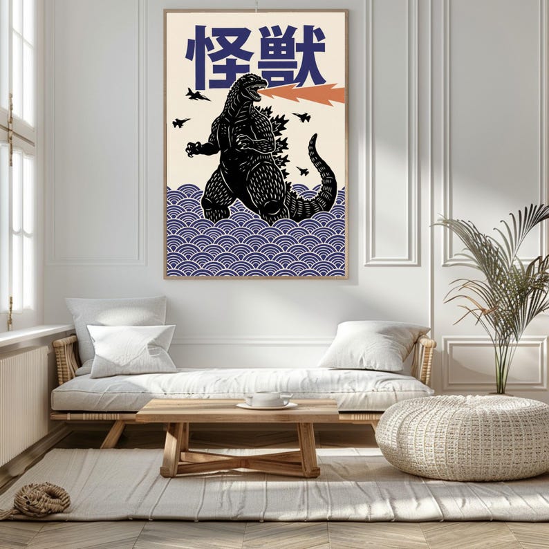 以下が含まれることがあります： 黒いゴジラのイラストとオレンジ色の火の息、日本語のテキストが描かれた額入りのアートプリント。アートワークは、青い波模様のクリーム色の背景に配置されています。プリントはリビングルームに展示されています。