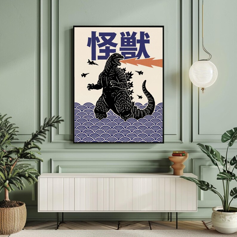 以下が含まれることがあります： ゴジラのイラストが描かれた、額入りのアートプリント。炎を吐くゴジラが、日本のテキストと青い波模様を背景に描かれています。戦闘機もいくつか含まれています。