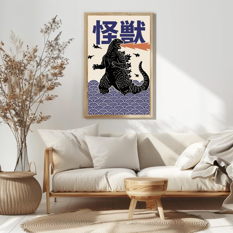 以下が含まれることがあります： 黒いゴジラのイラスト、オレンジ色の火の息、青色の日本語の「怪獣」の文字が描かれた額入りのアートプリント。アートワークは、青い波模様と小さな黒い飛行機のシルエットを配したクリーム色の背景に設定されています。