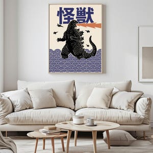 以下が含まれることがあります： 黒いゴジラのイラスト、オレンジ色の火の息、日本語のテキストが描かれた額入りのアートプリント。 作品はクリーム色の背景、青い波模様、小さな黒い飛行機のシルエットが特徴です。 部屋の装飾に最適です。