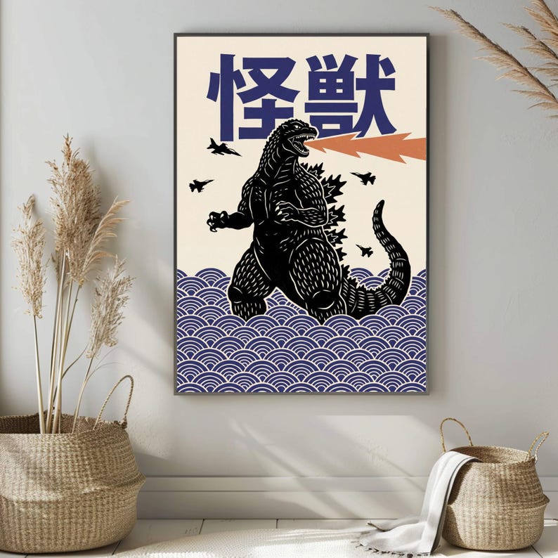 以下が含まれることがあります： クリーム色の背景に、オレンジ色の火を吐く黒いゴジラのイラストが描かれた額入りのアートプリント。 「モンスター」の日本語の文字は青色です。 下部には青い波模様があります。