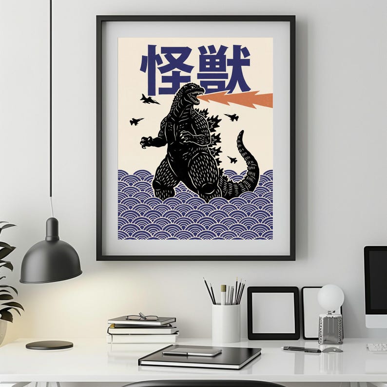 以下が含まれることがあります： 黒いフレームのアートプリント。オレンジ色の火を吐く黒いゴジラのイラストと、青色の日本語の「怪獣」の文字が特徴です。 作品は、青い波模様のクリーム色の背景に配置されています。