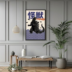 以下が含まれることがあります： 黒いゴジラのイラスト、オレンジ色の炎、日本語のテキストが描かれた額入りのアートプリント。アートワークは、青い波模様のクリーム色の背景に設定されています。