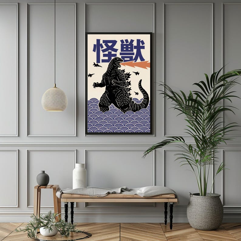 以下が含まれることがあります： 黒いゴジラのイラスト、オレンジ色の炎、日本語のテキストが描かれた額入りのアートプリント。アートワークは、青い波模様のクリーム色の背景に設定されています。