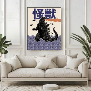 以下が含まれることがあります： 黒いゴジラのイラストが描かれた額入りのアートプリント。オレンジ色の火の息と日本語のテキストが特徴です。アートワークは、青い波模様のクリーム色の背景に設定されています。小さな黒い飛行機も含まれています。