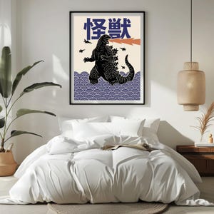 以下が含まれることがあります： 黒いゴジラのイラストが描かれた額入りのアートプリント。オレンジ色の火を吐き、日本語で怪獣と書かれています。アートワークは、青い波模様と黒い鳥が描かれたクリーム色の背景に配置されています。