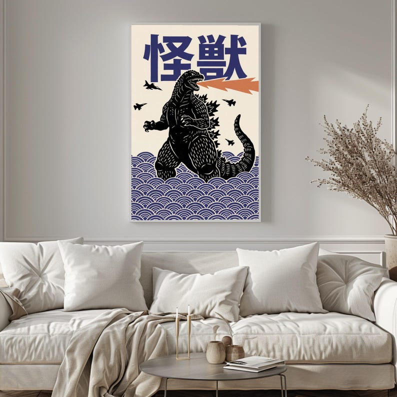 以下が含まれることがあります： 黒いゴジラのイラスト、オレンジ色の火の息、日本語のテキストが特徴の額入りアートプリント。アートワークは、青い波と小さな黒い飛行機を背景にクリーム色で設定されています。