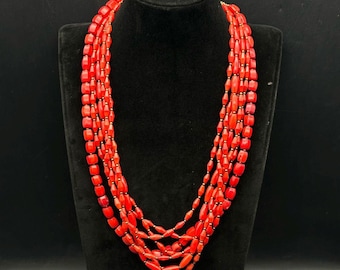 May include: A multi-strand necklace made of bright red coral beads. The necklace is made of several strands of beads, and the beads are all the same size and shape.