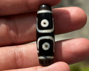 May include: A black and white agate bead with three white circles and a black outline. The bead is cylindrical and has a smooth, polished surface.