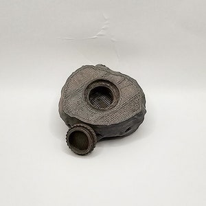 Puede incluir: Un peque&ntilde;o contenedor de forma de roca gris con una abertura redonda en la parte superior. El contenedor tiene una superficie texturizada y una peque&ntilde;a tapa redonda.