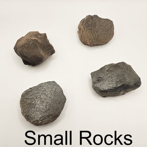 以下が含まれることがあります： 表面がテクスチャ加工された、不規則な形の小さな石が4つあります。石は、茶色と灰色が混ざり合った色合いです。石は白い背景に正方形に配置されています。石の下には「Small Rocks」という文字が書かれています。