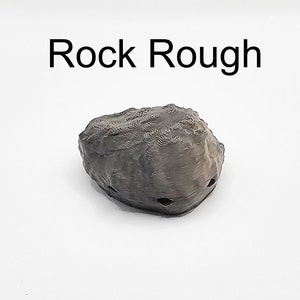 Puede incluir: Una roca rugosa de color gris oscuro con algunos agujeros. La roca est&aacute; sobre un fondo blanco. El texto "Rock Rough" est&aacute; por encima de la roca.