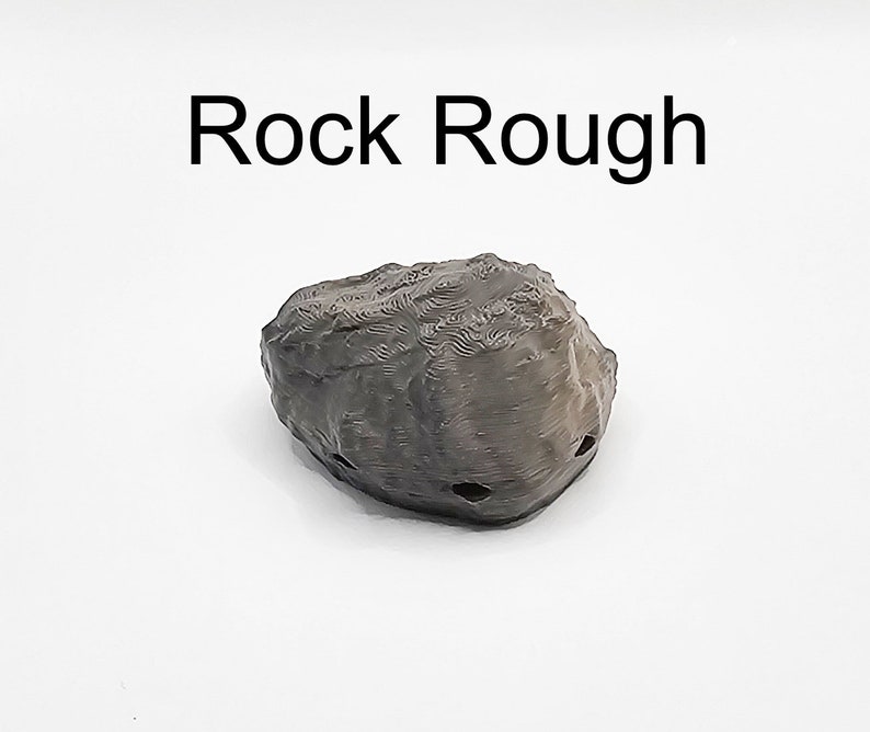 Puede incluir: Una roca rugosa de color gris oscuro con algunos agujeros. La roca est&aacute; sobre un fondo blanco. El texto "Rock Rough" est&aacute; por encima de la roca.