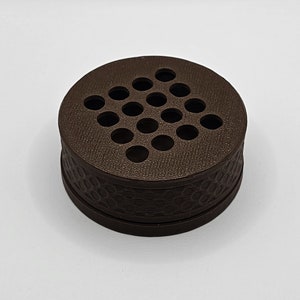 May include: A brown round container with a patterned base and a top with a grid of holes.