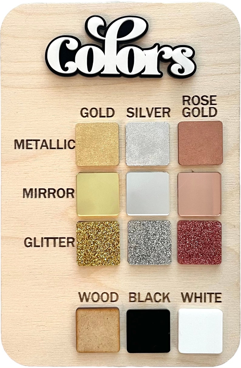 May include: A wooden board with the word "Colors" written in black and white lettering. The board displays a variety of color samples, including metallic gold, silver, rose gold, mirror gold, silver, rose gold, glitter gold, silver, rose gold, wood, black, and white.