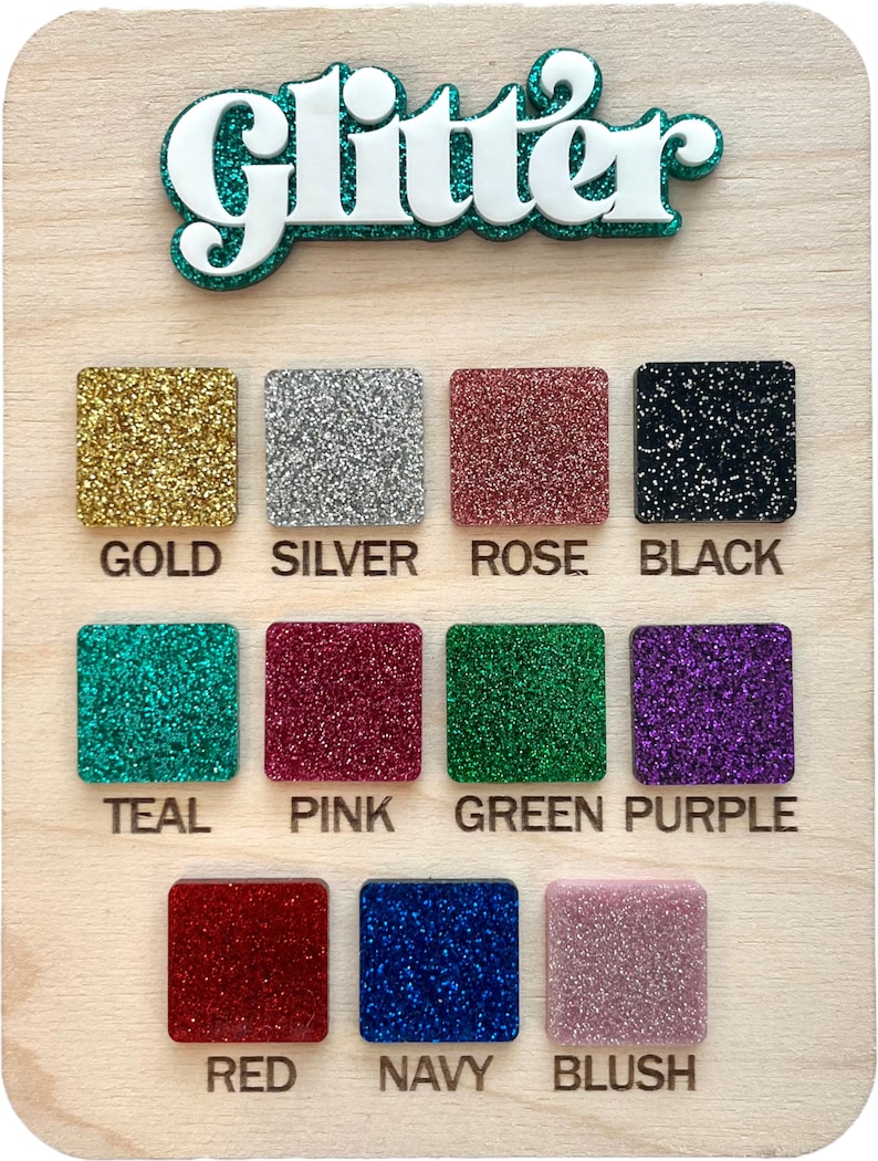 May include: A wooden board with the word "Glitter" in large white letters with a teal outline. The board displays a color chart of 12 different glitter colors, including gold, silver, rose, black, teal, pink, green, purple, red, navy, and blush.