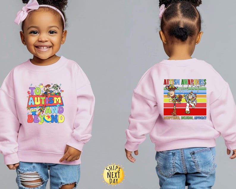 K&ouml;nnte beinhalten: Hellrosa Sweatshirt mit dem Text "TO AUTISM AND BEYOND" in bunten Buchstaben und einer Grafik von Zeichentrickfiguren. Auf der R&uuml;ckseite des Sweatshirts steht "AUTISM AWARENESS And Beyond" mit einem Regenbogenstreifen-Design und den Worten "ACCEPTANCE, INCLUSION, ADVOCACY".