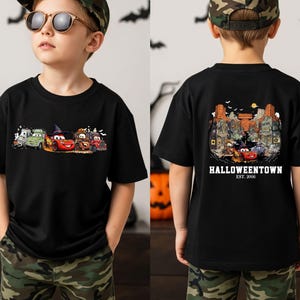 K&ouml;nnte beinhalten: Schwarzes T-Shirt mit einem Halloween-Motiv von Zeichentrickautos. Auf der Vorderseite sind Autos in Kost&uuml;men zu sehen, auf der R&uuml;ckseite eine Stadtszene mit dem Text "Halloweentown Est. 2006".