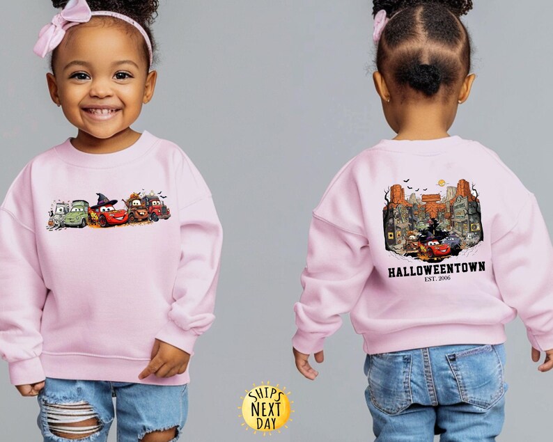 K&ouml;nnte beinhalten: Hellrosa Sweatshirt mit einem Halloween-Motiv von animierten Autos. Auf der Vorderseite sind mehrere Autos mit Halloween-Dekorationen abgebildet. Auf der R&uuml;ckseite ist eine gruselige Stadtlandschaft mit dem Text "Halloweentown" zu sehen.