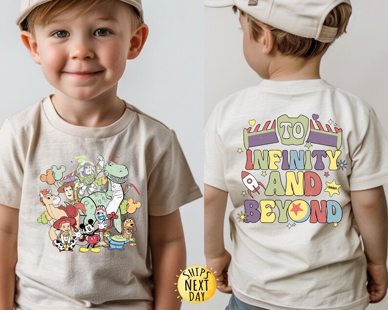 May include: A light beige t-shirt featuring a graphic print of Toy Story characters, including Woody, Buzz Lightyear, Rex, and a dinosaur. The back of the shirt displays the text "To Infinity and Beyond" in colourful letters.